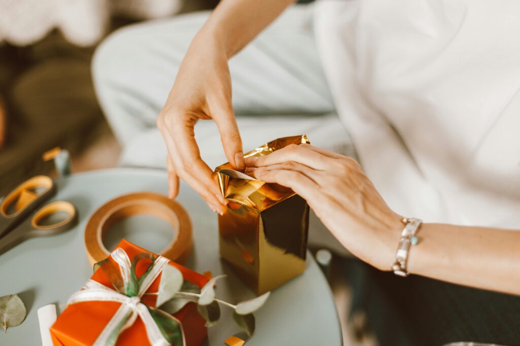 Hands wrapping gold and red presents in a cozy indoor setting, perfect for celebrations.find the perfect gift for every occasion